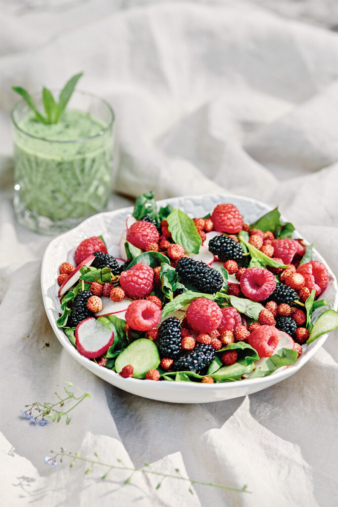 Салат из свежей зелени с ягодами в белой тарелке