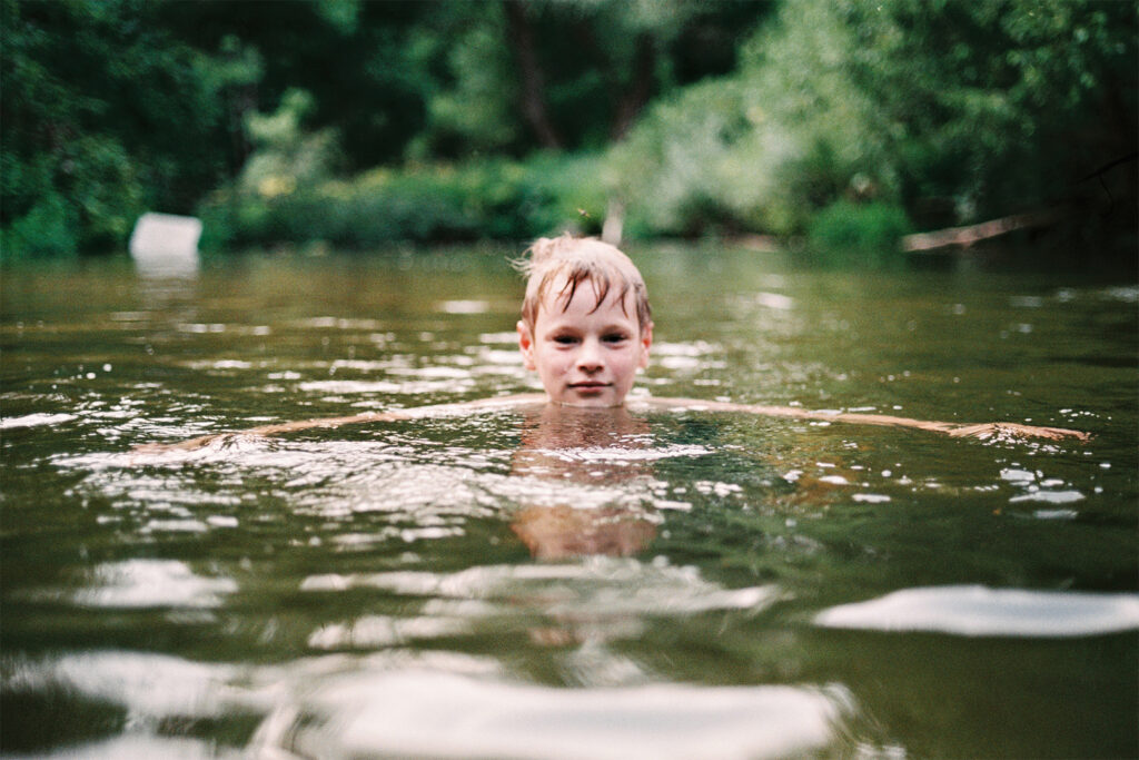 светловолосый мальчик плавает в реке