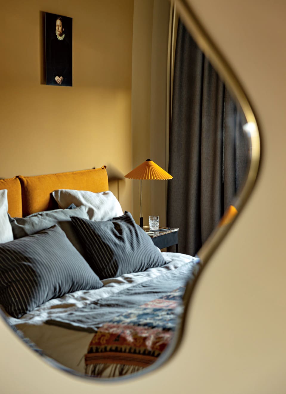 зеркало неровной формы и кровать в серых оттенках